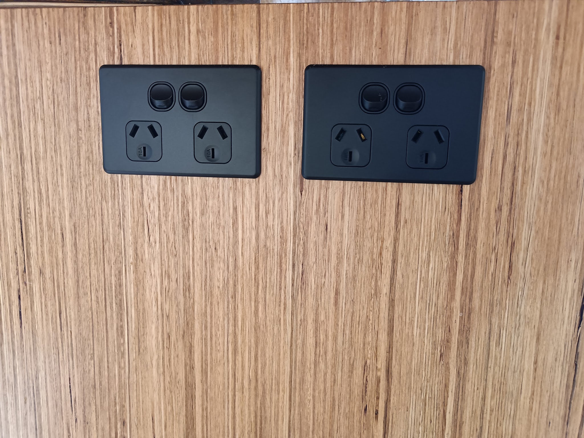Two matte black double power points installed on a timber wall