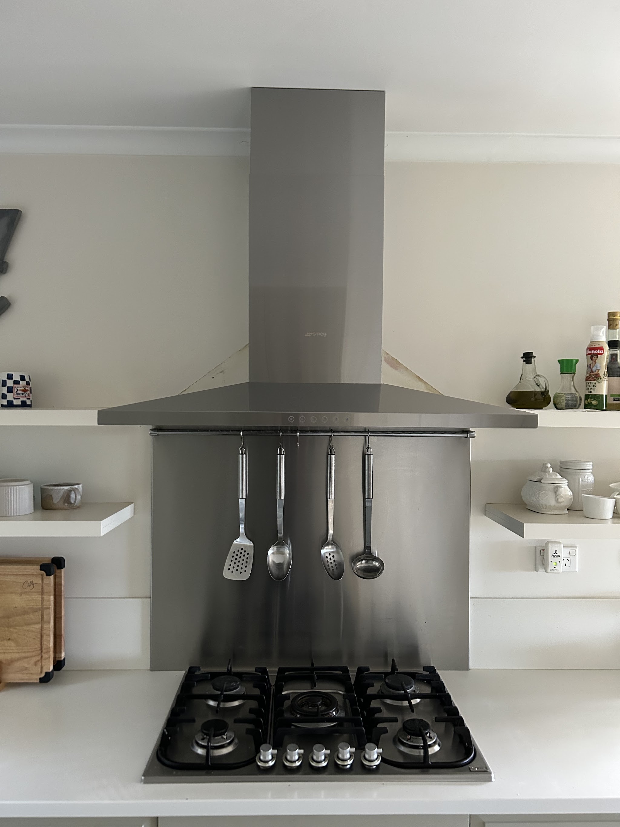 Stainless steel Smeg canopy rangehood above a five burner gas cooktop in a white kitchen